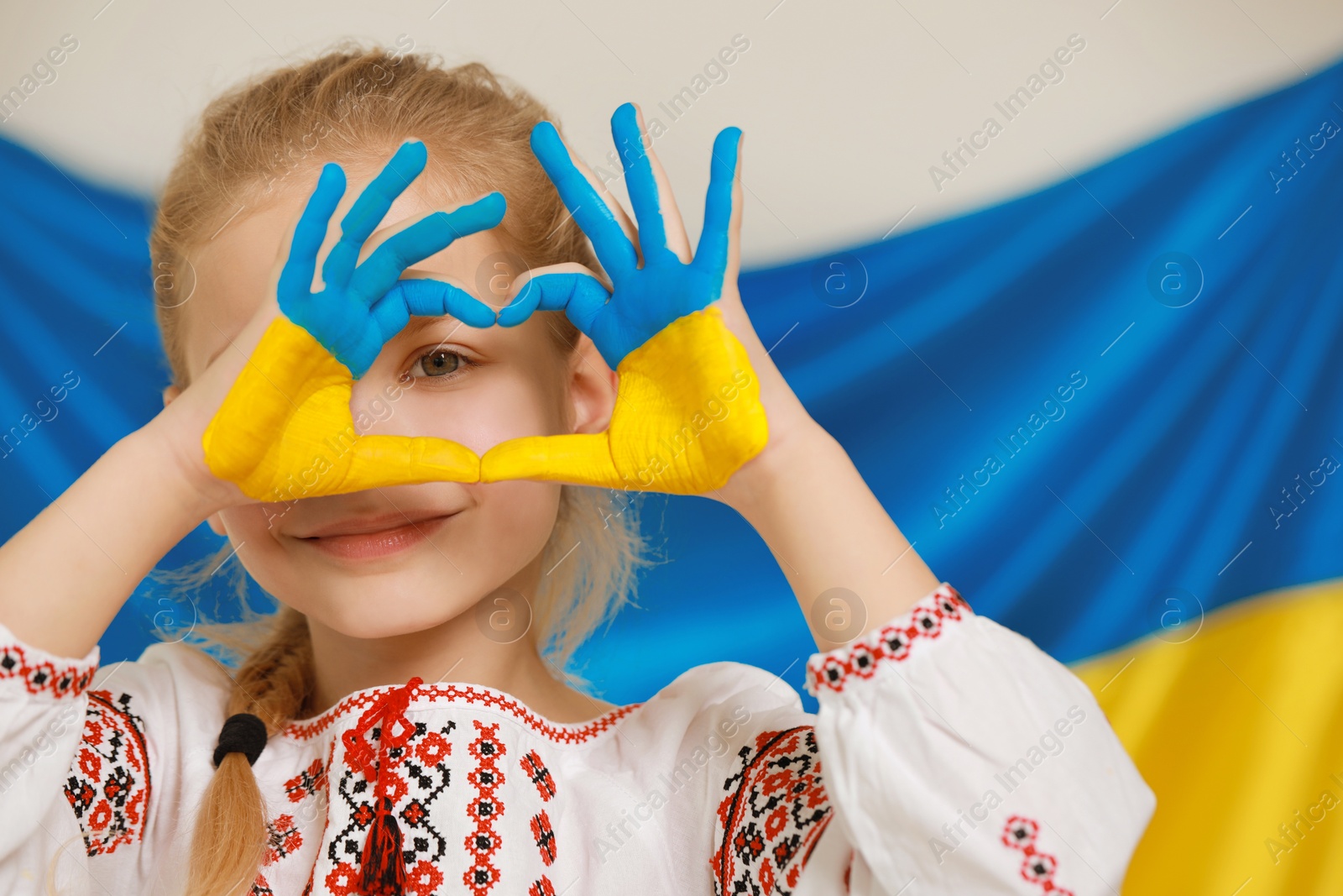 Photo of Little girl making heart with her painted hands near Ukrainian flag, space for text. Love Ukraine concept