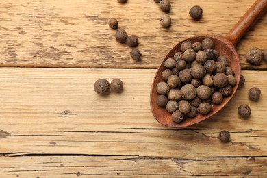 Dry allspice berries (Jamaica pepper) and spoon on wooden table, top view. Space for text
