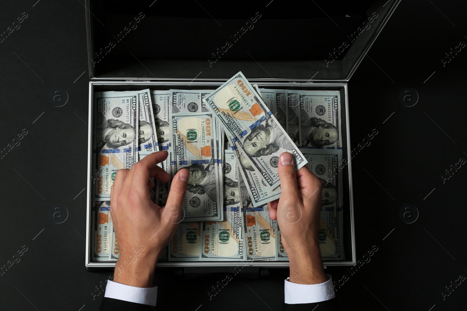 Photo of Businessman counting money over suitcase on dark background, top view