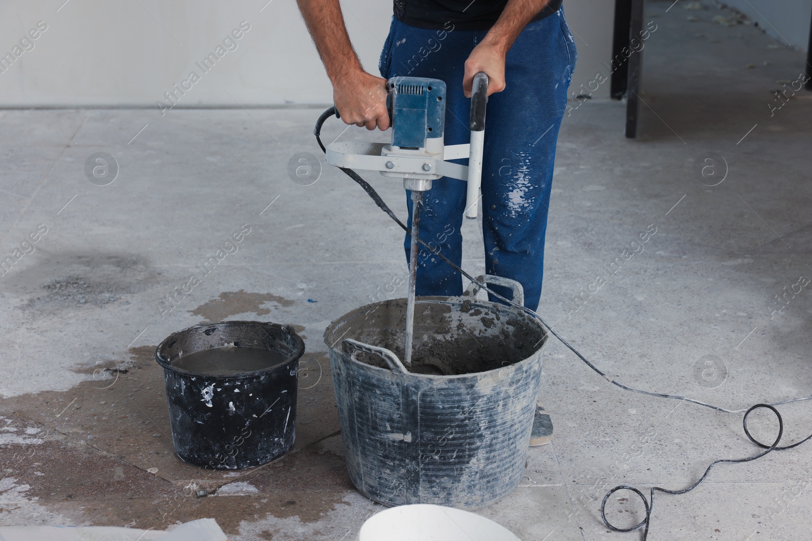 Photo of Professional worker mixing cement in bucket indoors, closeup. Tiles installation process