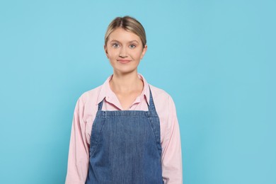 Beautiful young woman in denim apron on light blue background