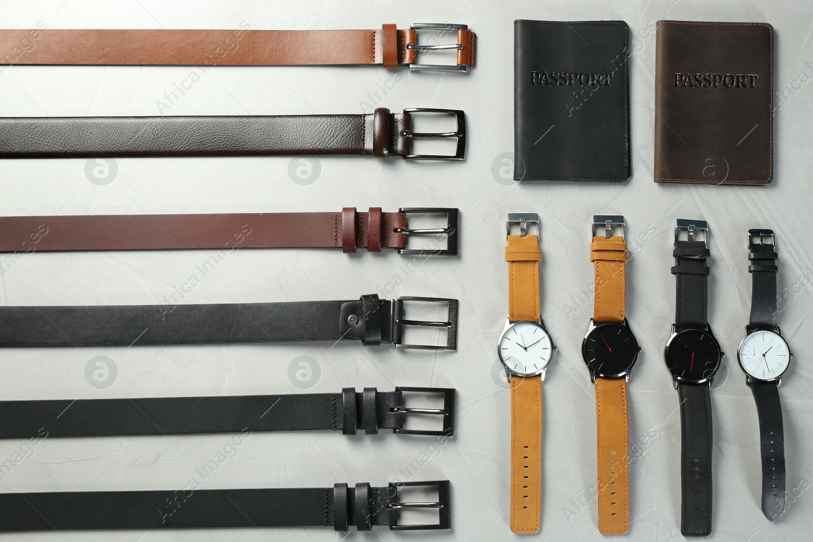 Photo of Leather belts, passports cases and wristwatches on grey stone table, flat lay