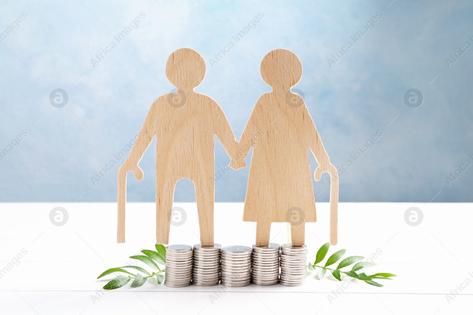 Photo of Pension savings. Figure of senior couple, stacked coins and green twigs on white wooden table