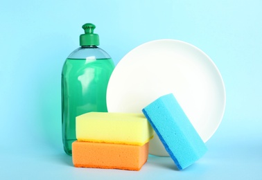 Photo of Cleaning supplies for dish washing and plate on light blue background