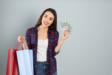 Photo of Young woman with money and shopping bags on light grey background. Space for text