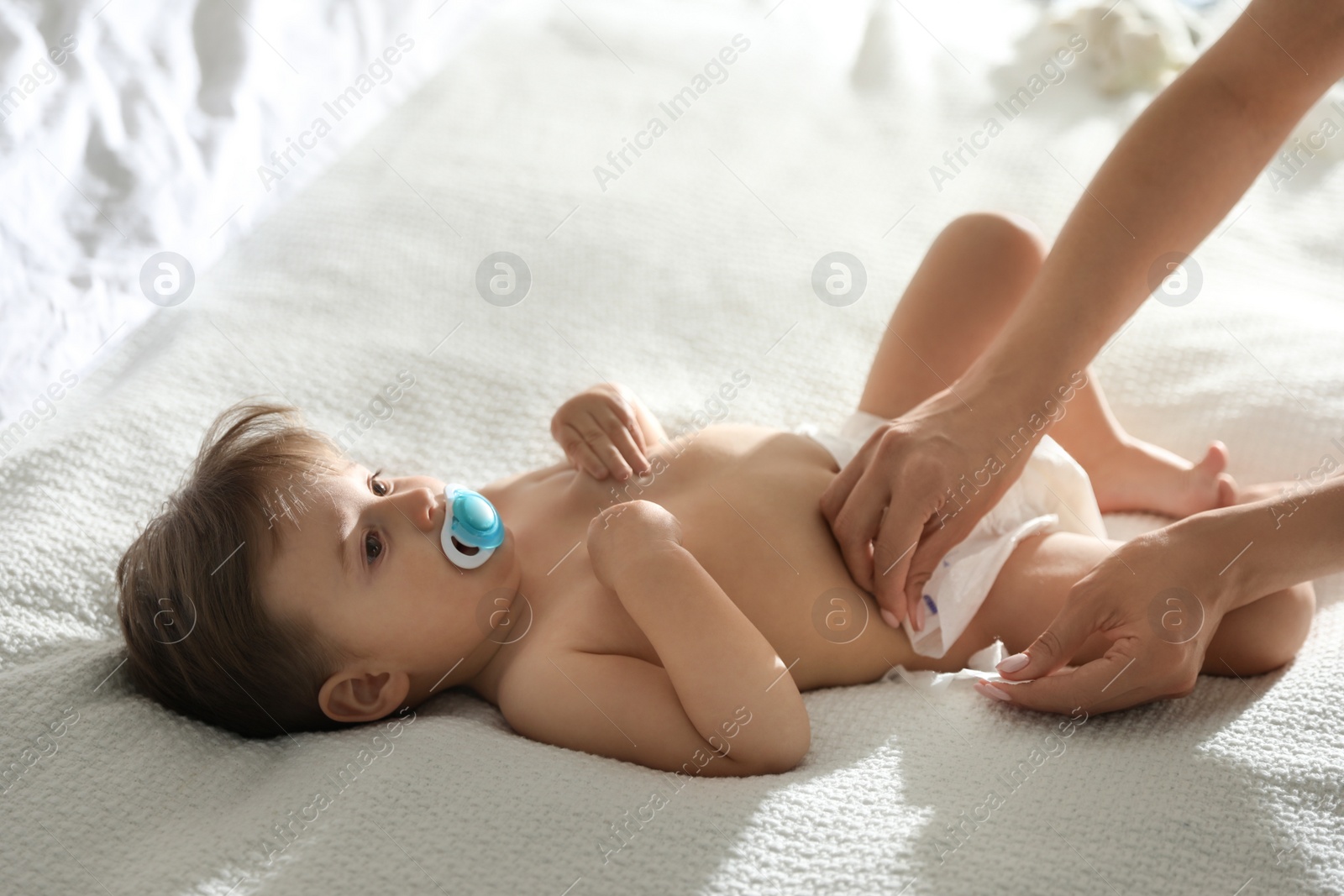 Photo of Mother changing baby's diaper on bed at home