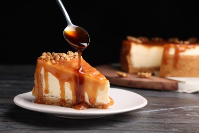 Photo of Pouring caramel sauce onto delicious piece of cheesecake with walnuts on black marble table, space for text
