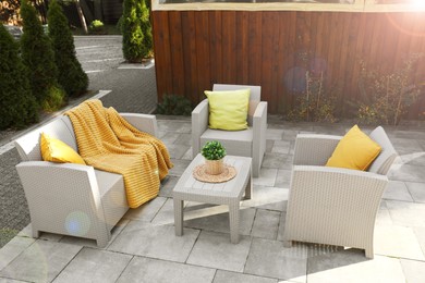 Beautiful rattan garden furniture, soft pillows, blanket and houseplant in backyard