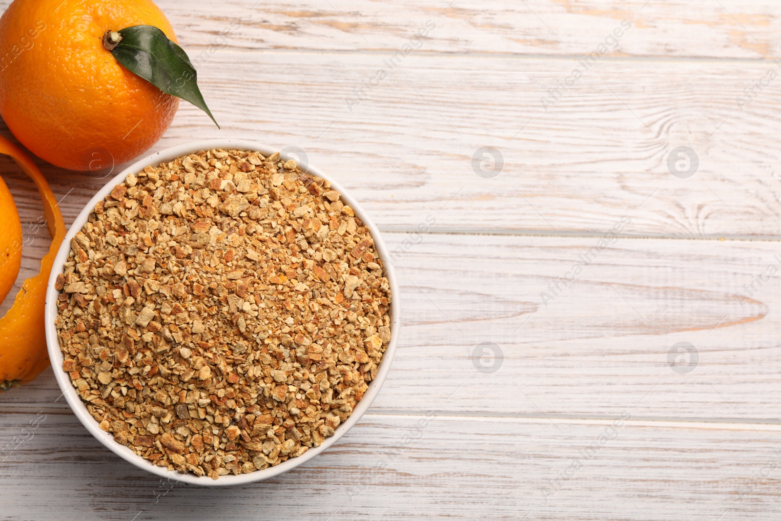 Photo of Bowl with dried orange seasoning zest and fruits on white wooden table, flat lay. Space for text