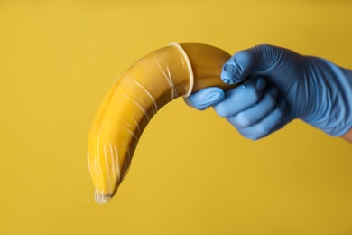 Photo of Doctor holding banana in condom symbolizing male sexual organ on yellow background, closeup. Potency problem