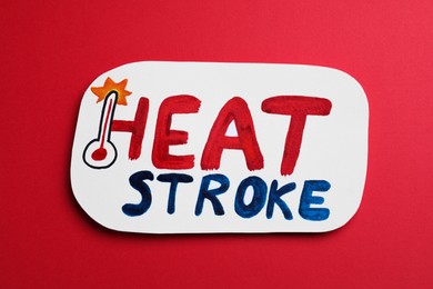 Photo of Card with words Heat Stroke and thermometer on red background, top view