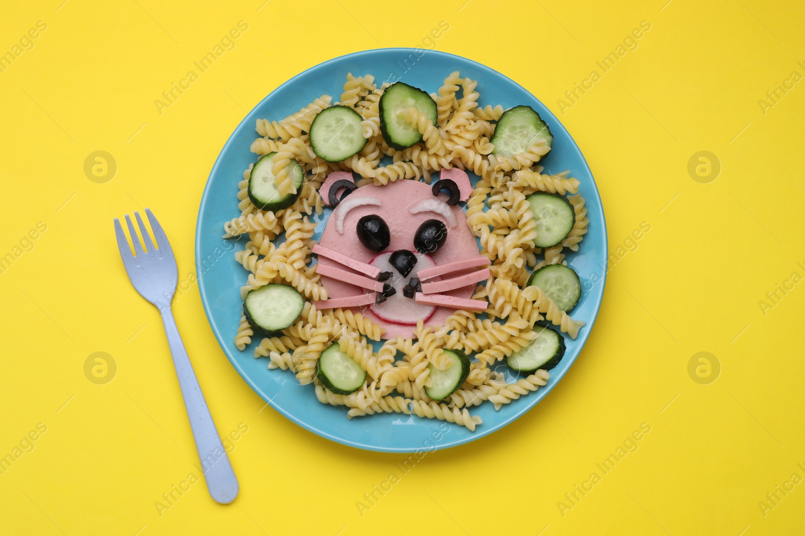 Photo of Creative serving for kids. Plate with cute bear made of tasty pasta, vegetables and sausage on yellow background, flat lay