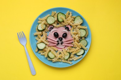 Photo of Creative serving for kids. Plate with cute bear made of tasty pasta, vegetables and sausage on yellow background, flat lay