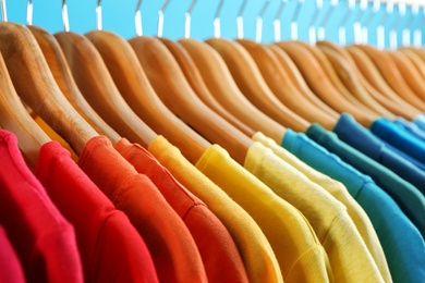 Hangers with bright clothes on blue background, closeup