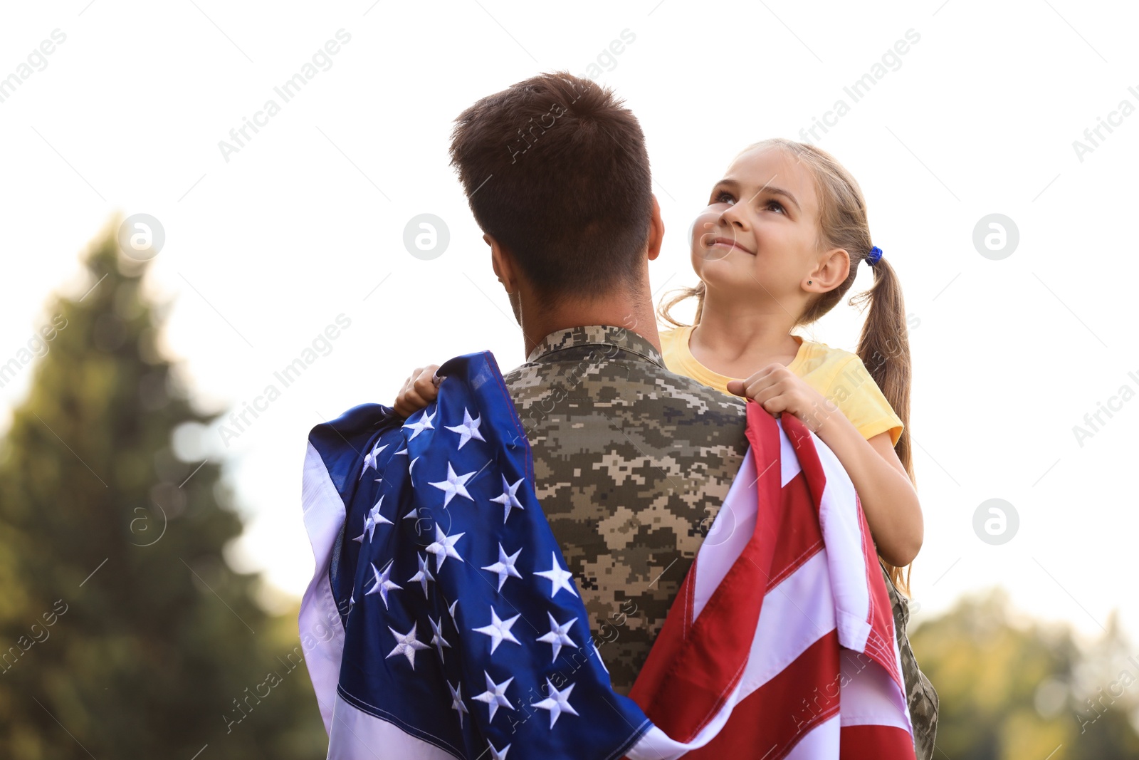 Photo of Father in military uniform with American flag and his daughter at sunny park