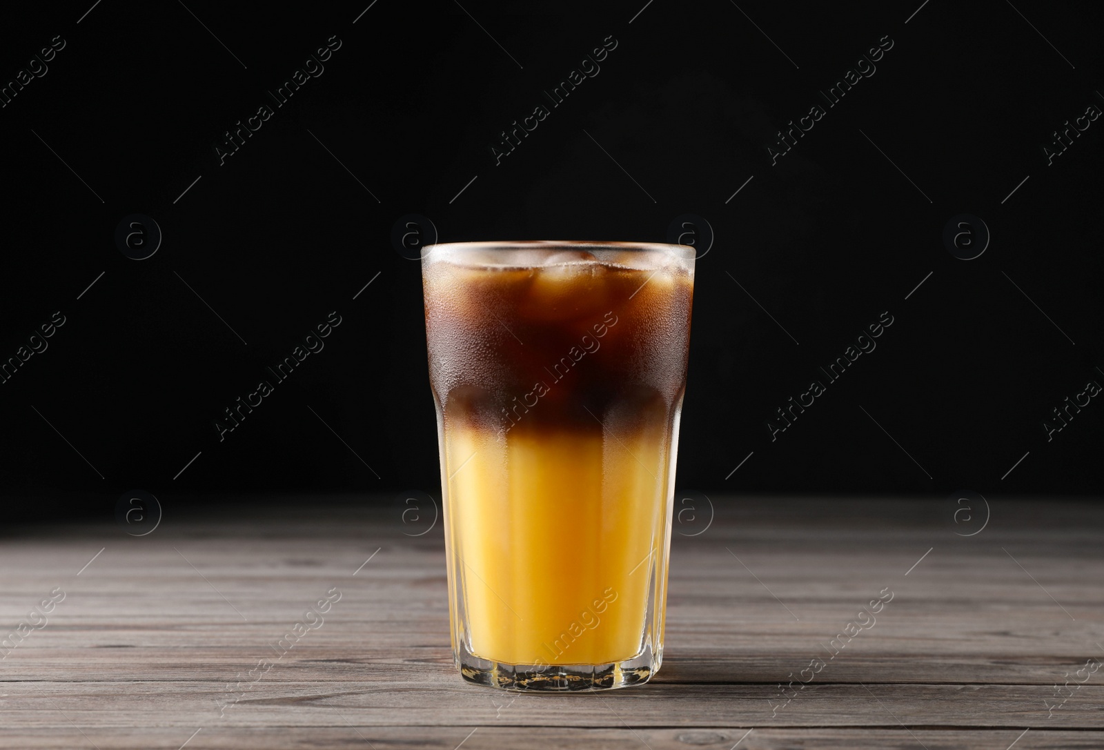 Photo of Tasty refreshing drink with coffee and orange juice on wooden table against dark background