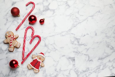 Tasty candy canes, Christmas balls and gingerbread cookies on white marble table, flat lay. Space for text