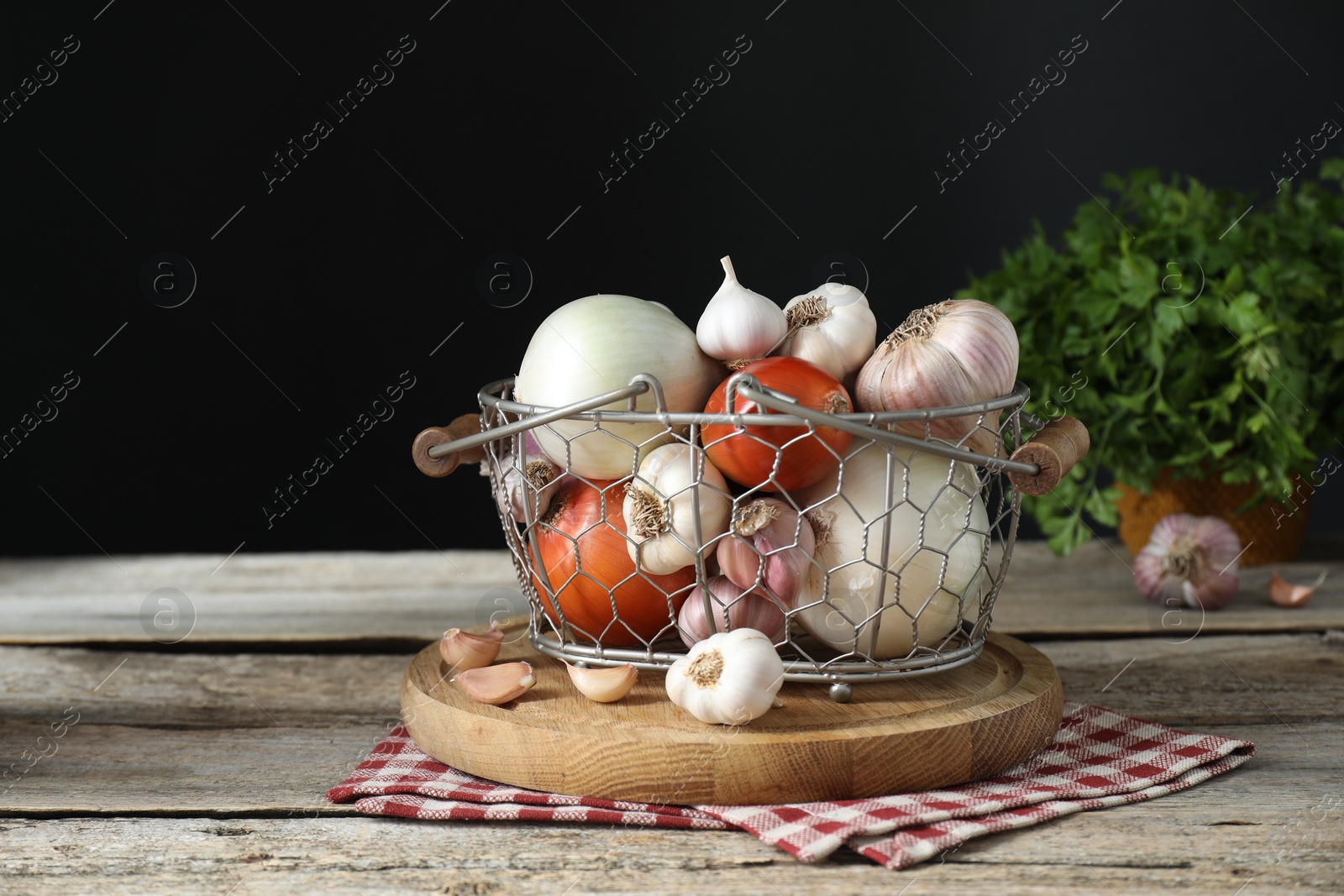 Photo of Fresh raw garlic and onions in metal basket on wooden table against black background, space for text