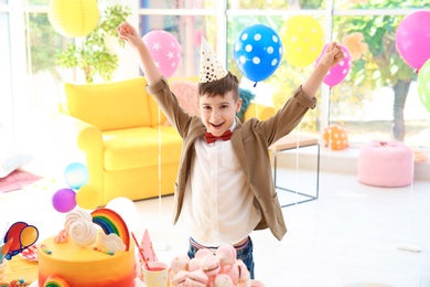 Photo of Cute little boy near table with treats at birthday party indoors