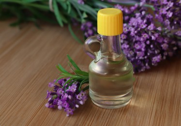 Photo of Bottle of natural essential oil and lavender flowers on wooden table, closeup