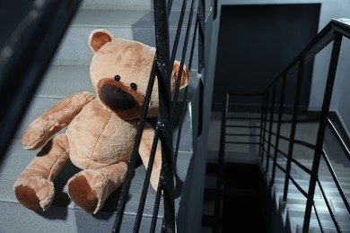 Photo of Lonely teddy bear on staircase near metal railing indoors
