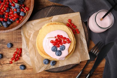 Tasty pancakes with natural yogurt, blueberries and red currants on wooden table, flat lay