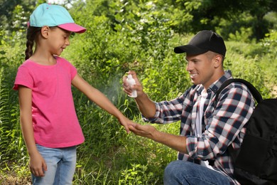 Father spraying tick repellent on his little daughter's arm during hike in nature