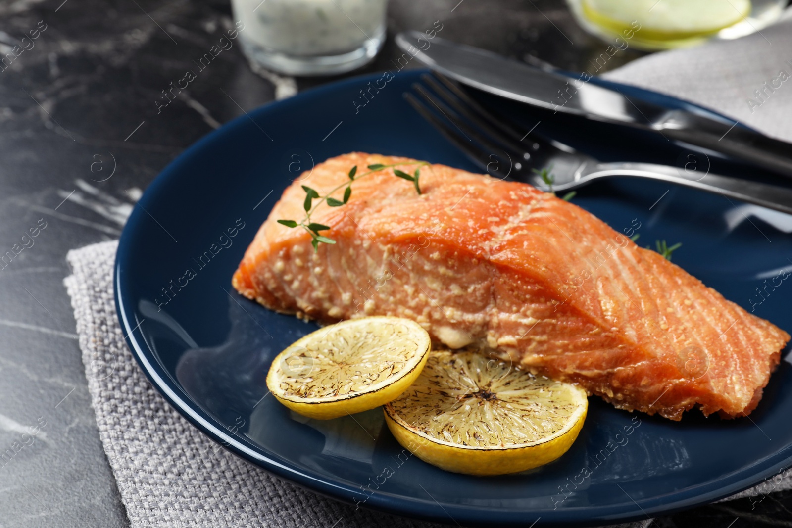 Photo of Tasty cooked red fish with lemon on dark marble table, closeup