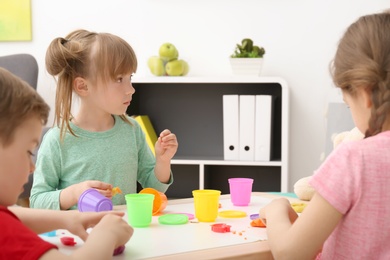 Cute little children using play dough at table indoors