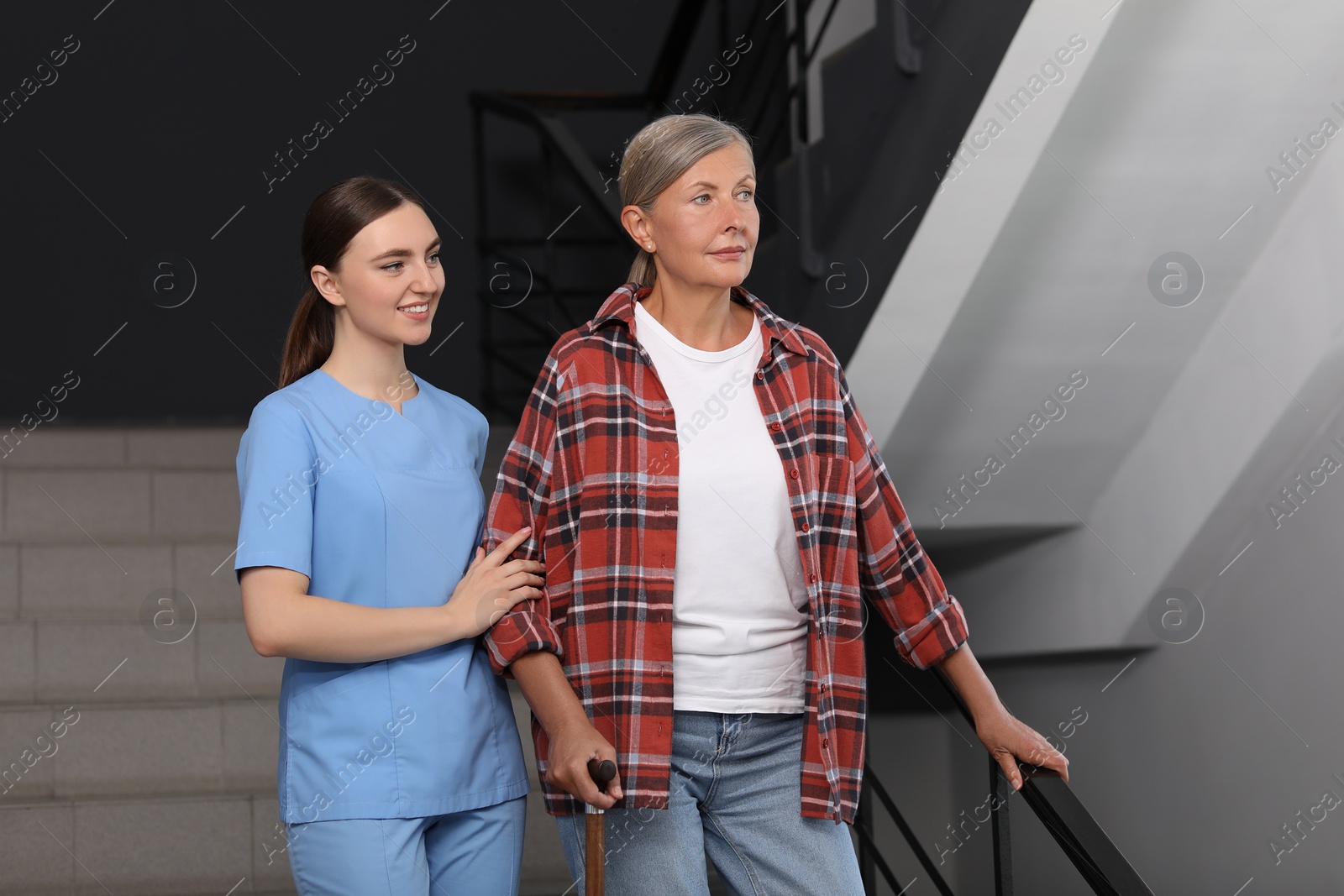 Photo of Young healthcare worker assisting senior woman on stairs indoors