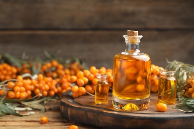 Photo of Natural sea buckthorn oil and fresh berries on wooden table. Space for text