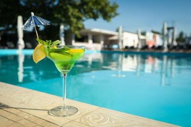 Photo of Tasty refreshing cocktail on edge of swimming pool. Party drink
