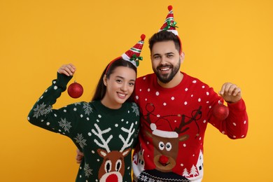 Photo of Happy young couple in Christmas sweaters holding festive baubles on orange background
