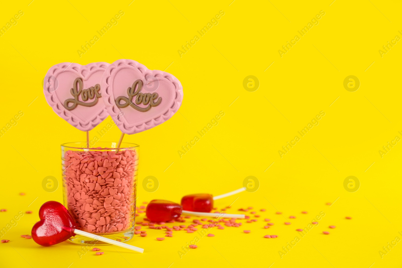 Photo of Heart shaped lollipops made of chocolate and sugar syrup with sprinkles on yellow background. Space for text