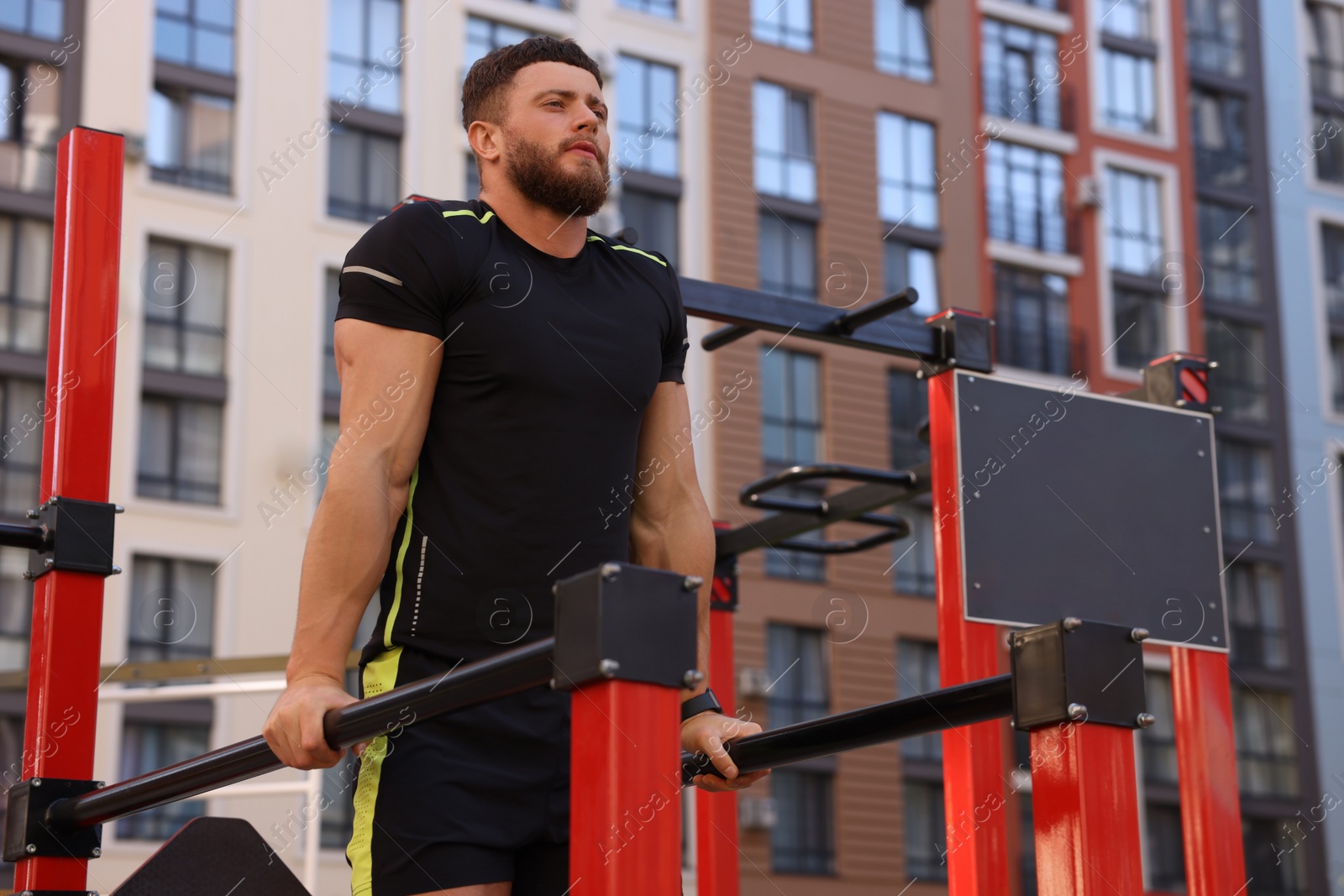 Photo of Man training on parallel bars at outdoor gym, low angle view