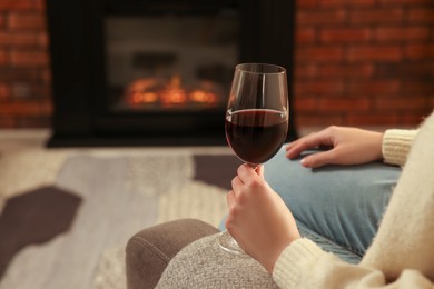 Photo of Woman with glass of wine near fireplace at home, closeup. Space for text