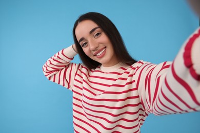 Photo of Smiling young woman taking selfie on light blue background