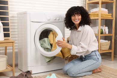 Photo of Woman putting laundry into washing machine indoors