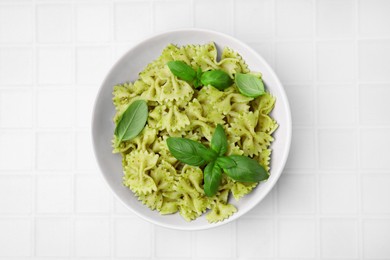 Delicious pasta with pesto sauce and basil on white tiled table, top view