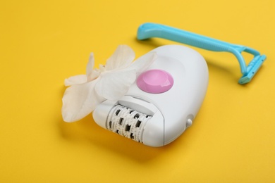 Modern epilator, orchid flower and shaving razor on yellow background