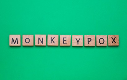 Photo of Word Monkeypox made of wooden squares on green background, top view