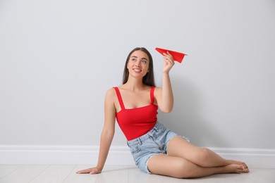 Photo of Beautiful young woman playing with paper plane near light grey wall