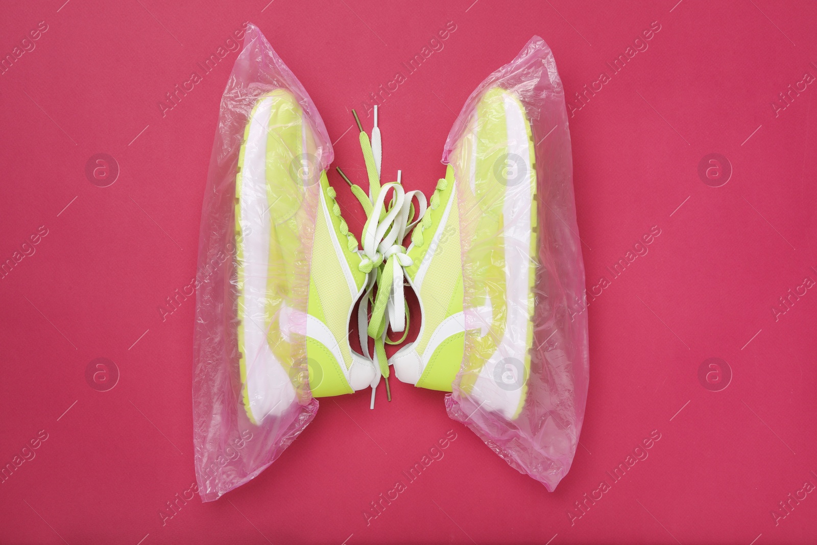 Photo of Sneakers in shoe covers on pink background, top view