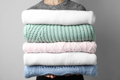 Photo of Woman holding stack of warm clothes on grey background, closeup. Autumn season