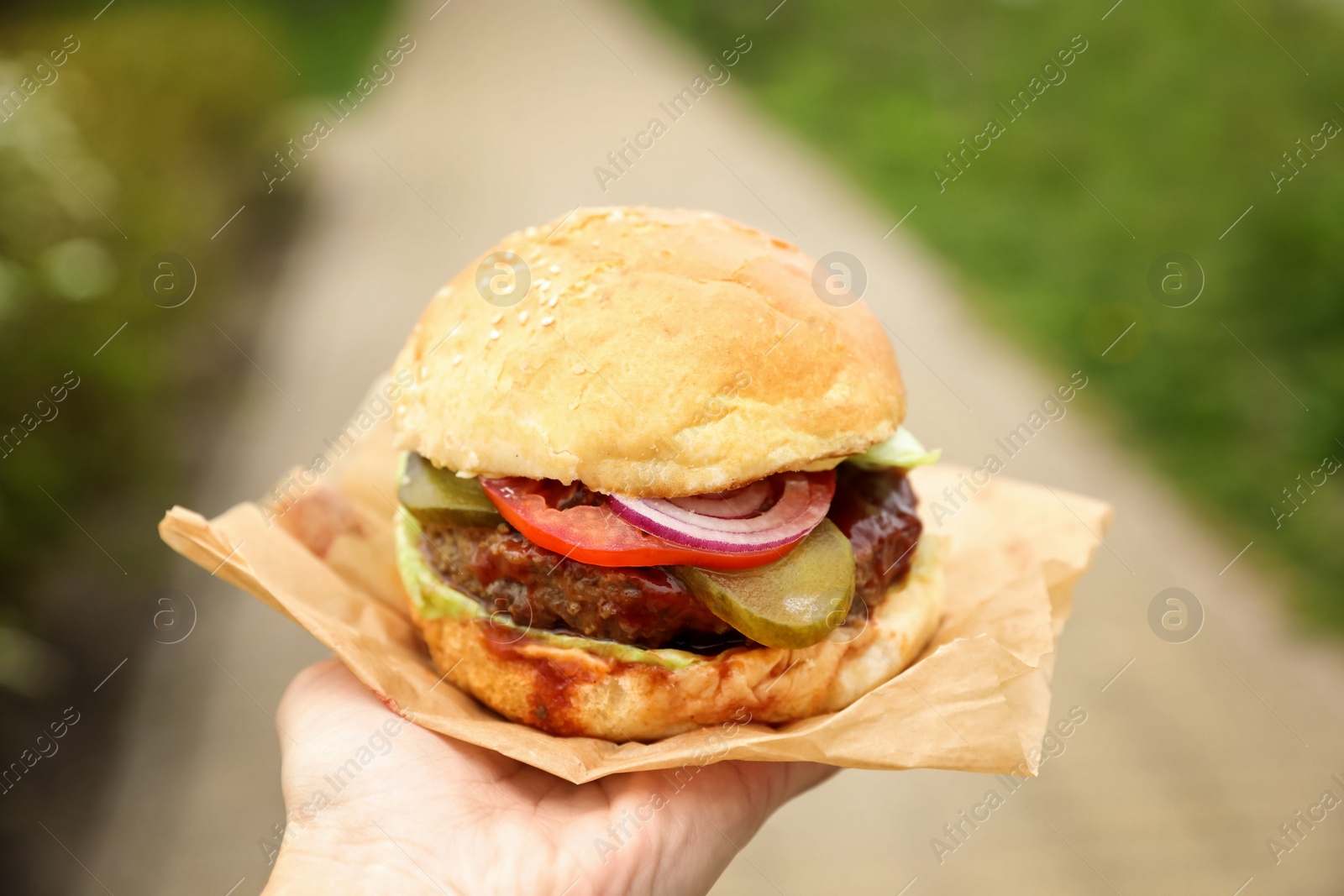 Photo of Little girl holding fresh delicious burger outdoors, closeup. Street food