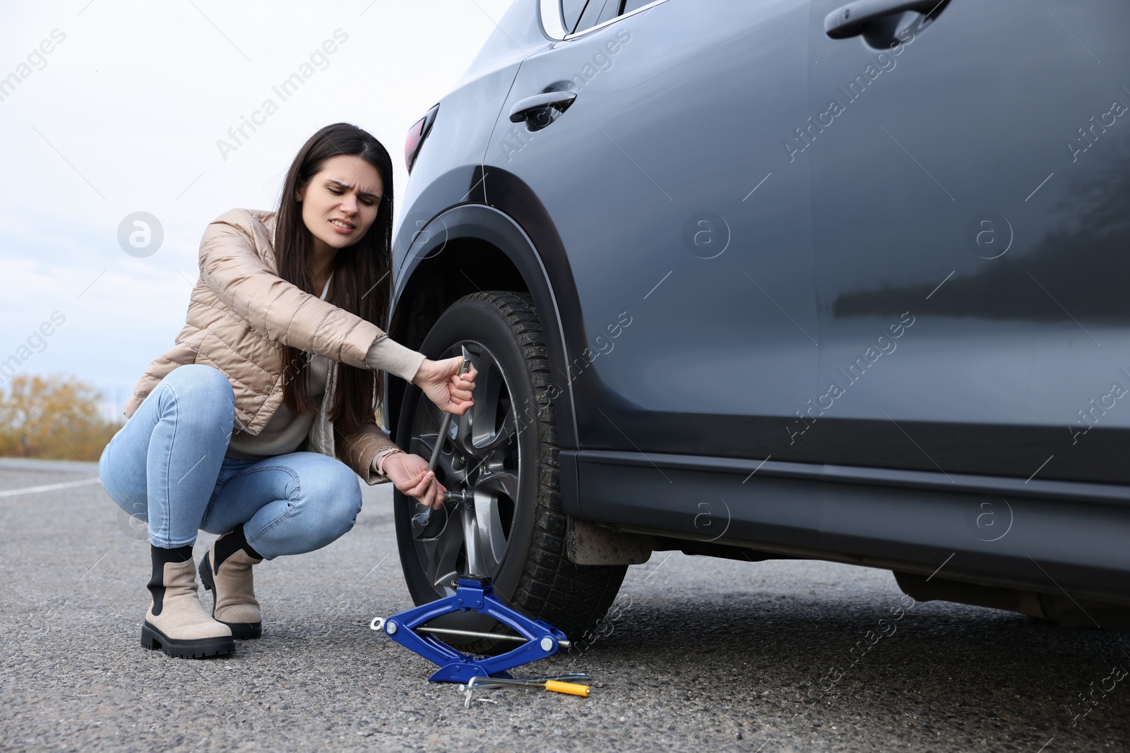 Photo of Worried young woman changing tire of car on roadside