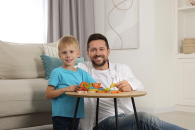 Motor skills development. Happy father helping his son to play with colorful wooden arcs at coffee table in room