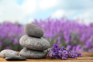 Photo of Spa stones and fresh lavender flowers on wooden table outdoors, closeup. Space for text