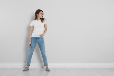 Young woman in stylish jeans near light wall. Space for text