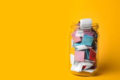 Photo of Glass jar full of folded paper sheets on yellow background, space for text